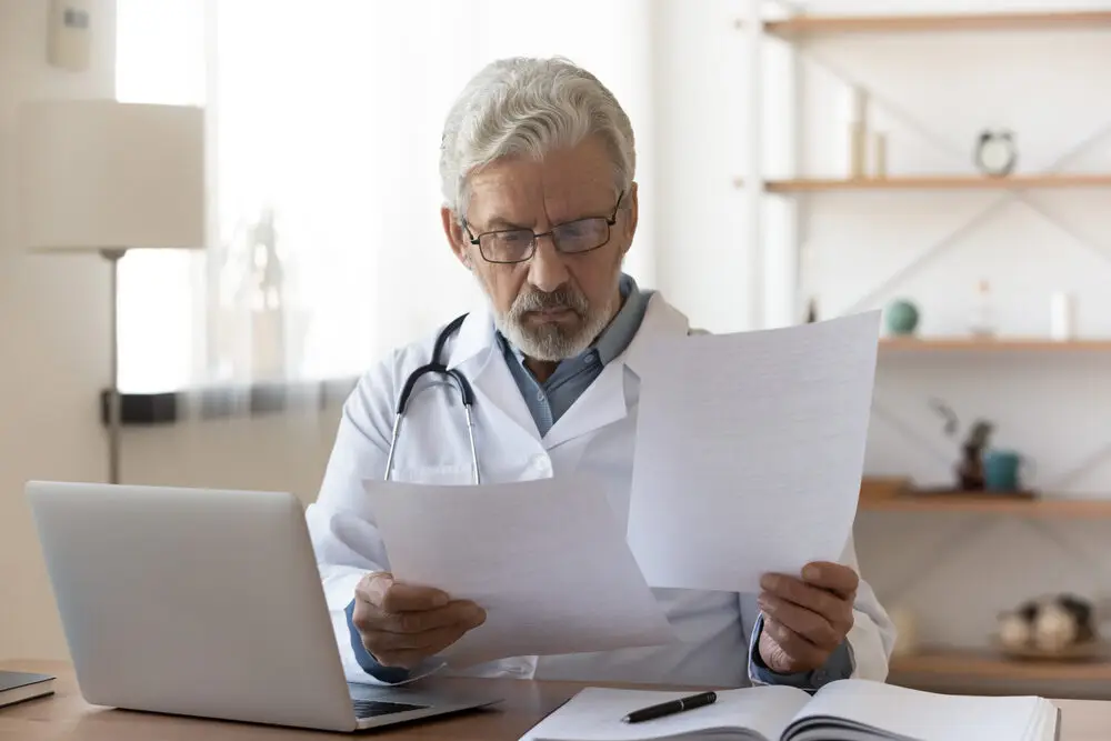 Serious Professional Senior Elderly Doctor Doing Paperwork